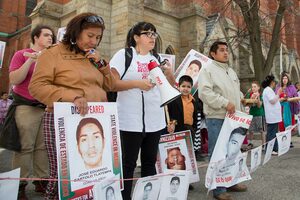 Family members stand holding signs to bring awareness of the Ayotzinapa case