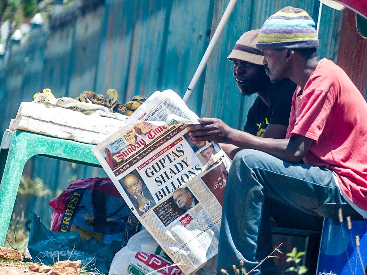 Two South African men read a newspaper detailing another financial scandal involving the Gupta family, October 2016 (the month when South Africa's minister of justice stated in court documents that the brothers were involved in suspicious transactions to the tune of several billion Rand). Photo CC BY-NC-ND 2.0: Skatkat / Flickr. Some rights reserved.]