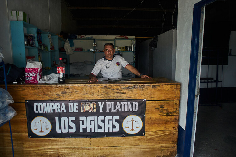 A man sits behind a counter with a sign saying that he buys gold.