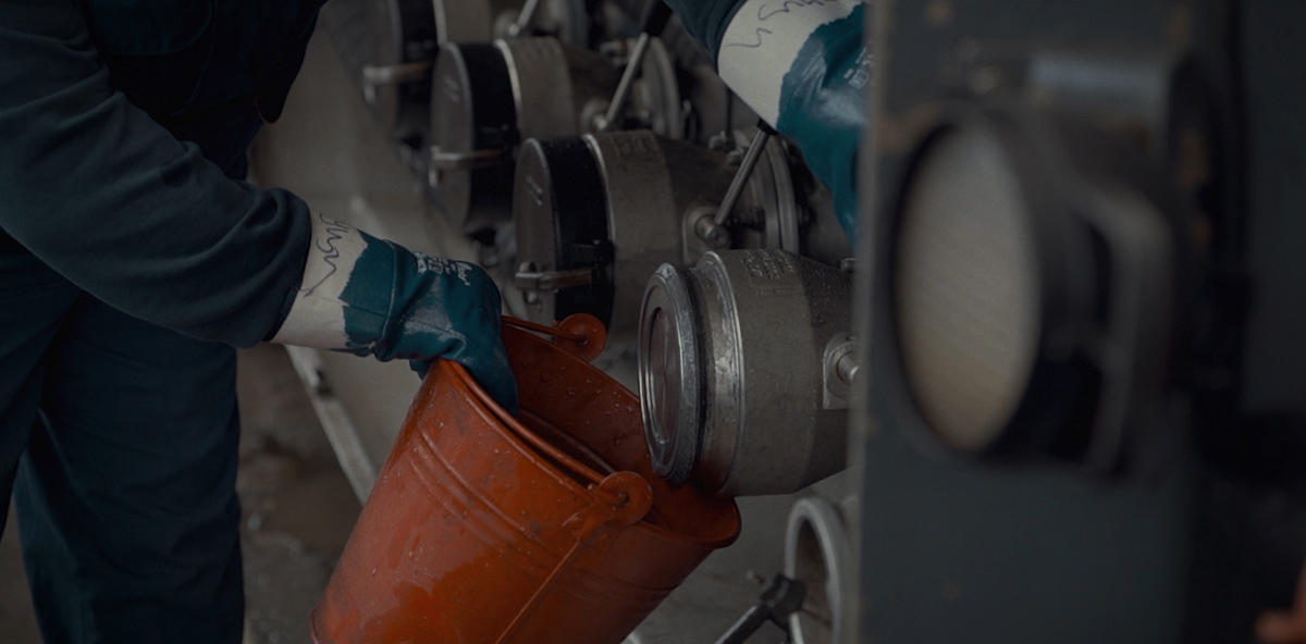 A worker uses a bucket to collect a sample of oil.