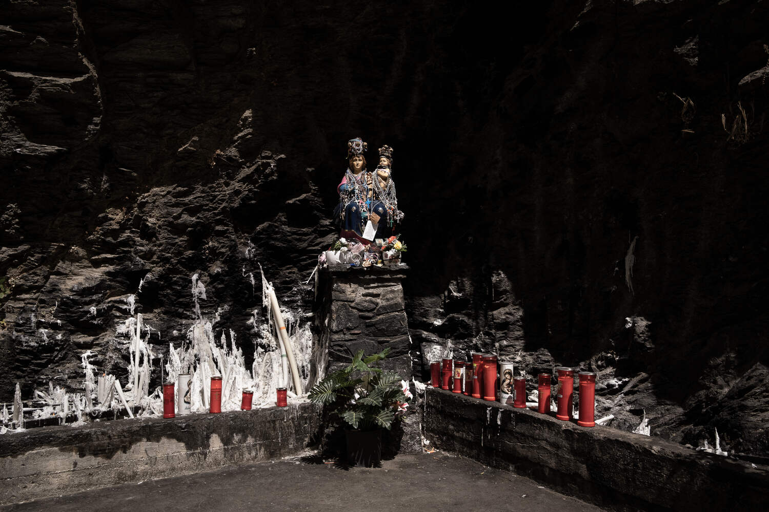 A colorful statue of the Madonna and Child on a stone pedestal in a cave.