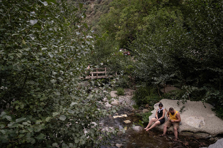 A mountain stream where a man and a woman are washing their feet sitting on a large rock.