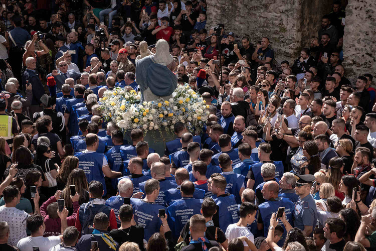 A sea of people watches a procession of men wearing matching blue t-shirts carrying the Madonna and Child away from the camera.