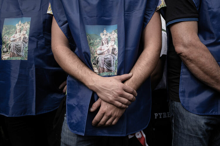 A close-up of the chest of three men, who are wearing blue nylon tabards, with a stylized photo of the Madonna and Child wearing crowns in the middle.