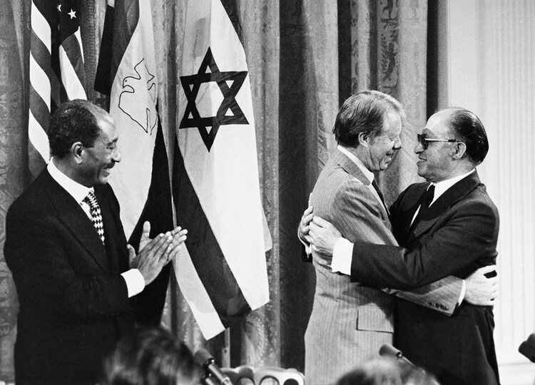 President Anwar Sadat applauds as President Jimmy Carter embraces Prime Minister Menachem Begin