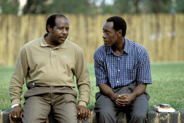 Paul Rusesabagina and Don Cheadle sitting on a low wall, talking