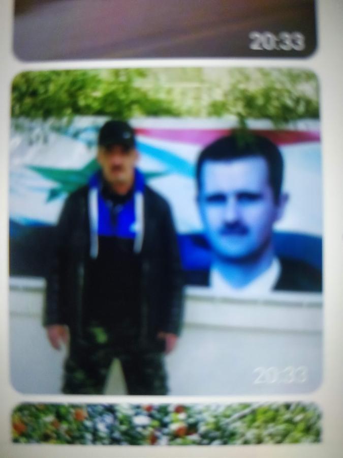 A low-quality thumbnail extracted from Amelchenko’s phone shows him posing in front of a poster of Syrian President Bashar Assad.