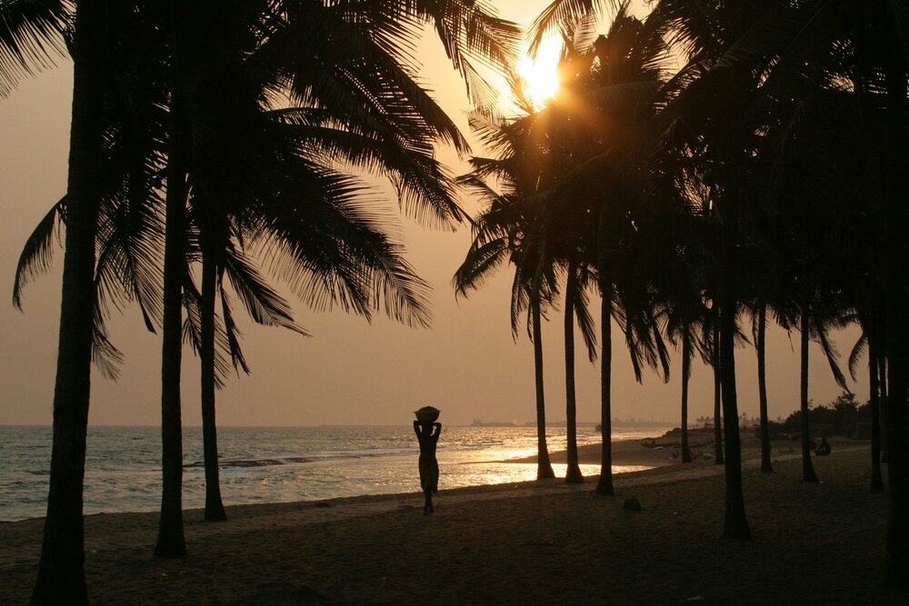 Silhouetted palm trees and a woman carrying a basket on the beach at Lomé, Togo in the Gulf of Guinea